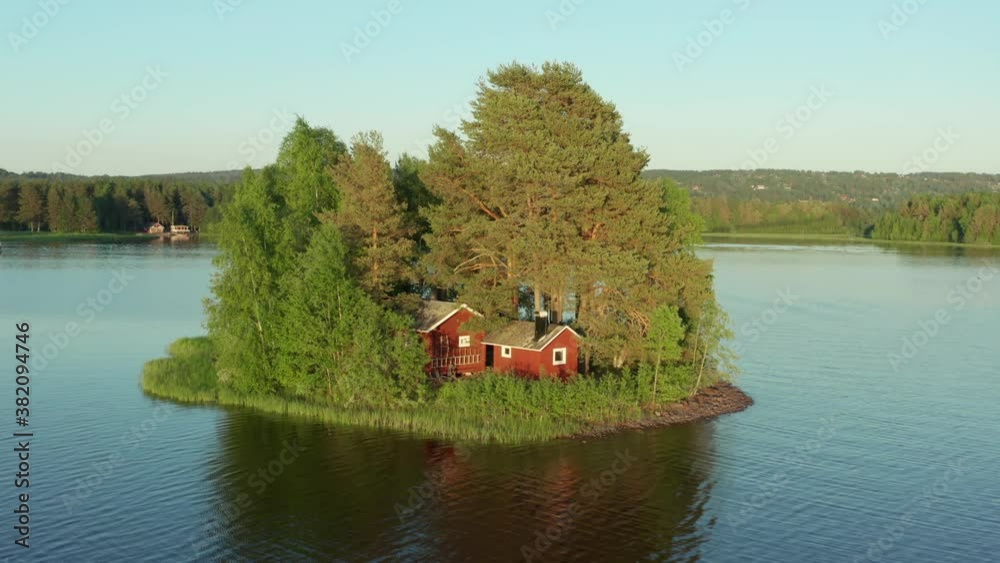 Red cabin on island. Sweden summer house in lake tiny remote between trees. Cute little wooden Swedish home with beach. Picturesque cottages in aerial drone shot on beautiful summer evening