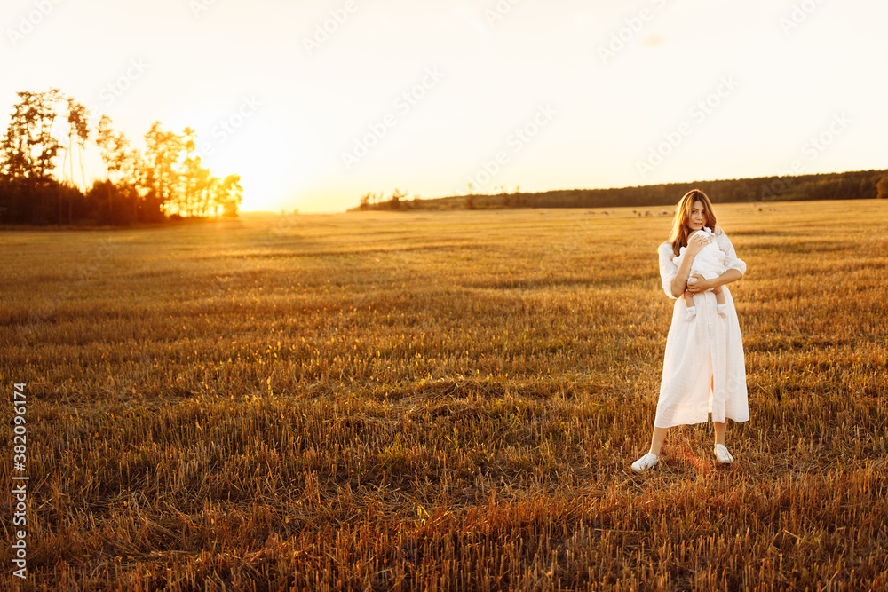 Elegant woman with beautiful newborn baby girl walking at the field, lovely mom hold in arms cute little daughter, enjoy happy family moments, parenting and maternity concept