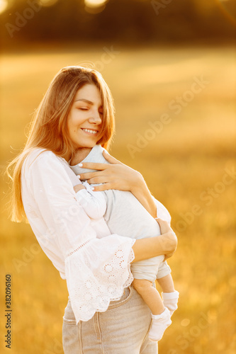 Adorable woman with beautiful newborn baby girl at the field, happy mom hold cute little daughter in arms, smiling, enjoy every moment of parenting, maternity concept 