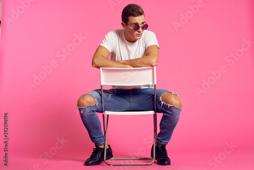 A man sits on a chair in a white t-shirt and jeans modern style pink isolated background