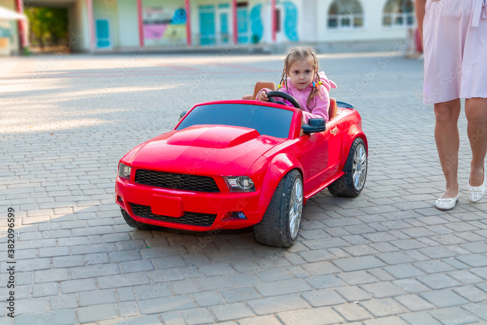 little beautiful girl rides in the park on a red electric machine on a summer day little beautiful girl rides in the park on a red electric machine on a summer day