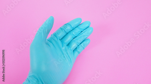 Close up of left hand wear latex glove on pink background.
