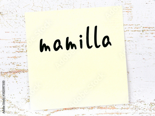 Yellow sticky note on wooden wall with handwritten word mamilla photo