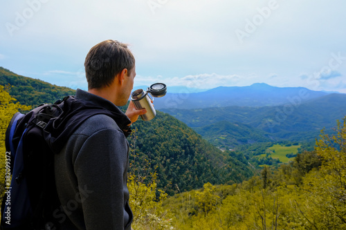 Man, hiker drinking beverage from a thermos in the mountains. Traveler with backpack. Equipment for trekking. Natural background. Copy space. High-quality photo