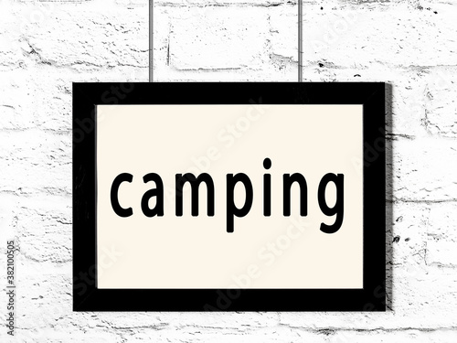 Black frame hanging on white brick wall with inscription camping