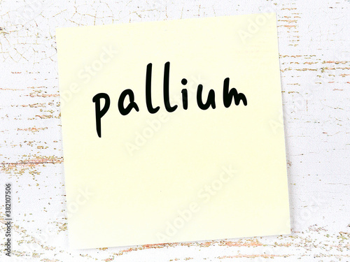 Yellow sticky note on wooden wall with handwritten word pallium photo