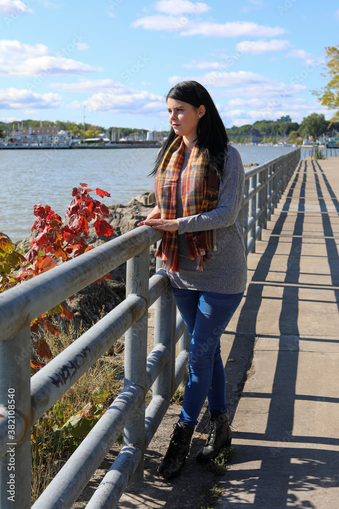Smiling young woman walking on a pier. Sunny autumn morning with a view of the river.