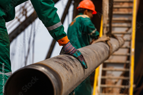 Tableau sur toile Two oil workers in green and orange work wear and suede gloves  with  rusted drilling pipe
