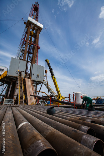 Works on drilling rig on oil deposit. Rusted drilling pipes and oil worker on foreground. Blue sky and light clouds. Wide-angle photo..