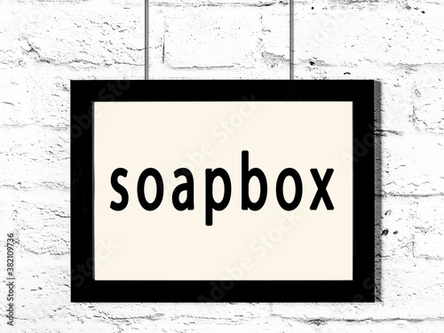 Obraz na plátně Black frame hanging on white brick wall with inscription soapbox