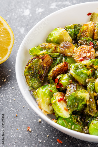 Close up on roasted / fried brussels sprouts in a white bowl with chili and garlic flakes seasoning. Fresh and cooked seasonal food.