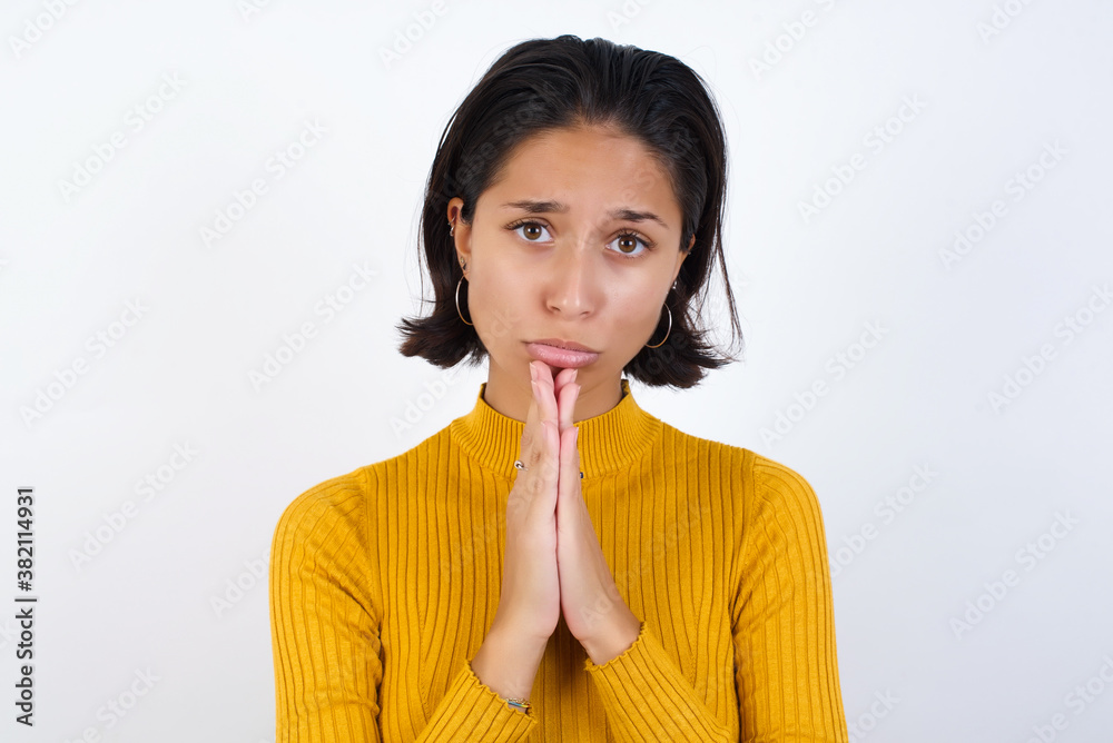 Positive Young hispanic girl with short hair wearing casual yellow sweater isolated smiles happily, glad to receive pleasant news from interlocutor, keeps palms together, People emotions concept. Positive Young hispanic girl with short hair wearing casual yellow sweater isolated smiles happily, glad to receive pleasant news from interlocutor, keeps palms together, People emotions concept.