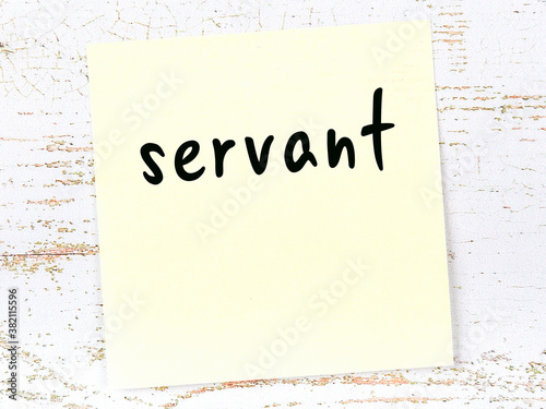 Yellow sticky note on wooden wall with handwritten word servant