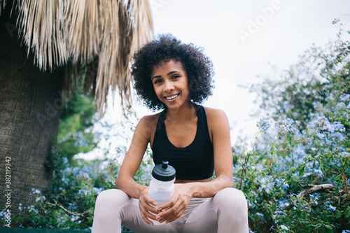 Cheerful ethnic woman resting after workout and drinking water