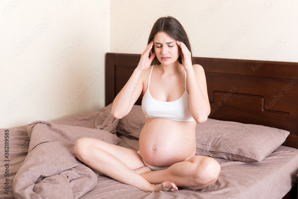 Young pretty pregnant woman suffering from headache at home in bed Young pretty pregnant woman suffering from headache at home in bed