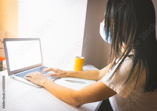 Side view of black haired girl in white shirt and medical mask on sitting at home and typing on keyboard. Study at home concept photo