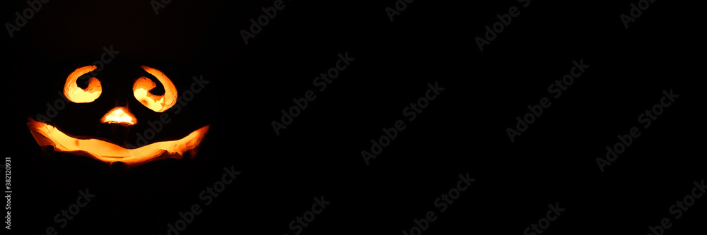 Fototapeta premium glowing smiling face Halloween pumpkin, candle holder, isolated on night dark black background. space for text. banner