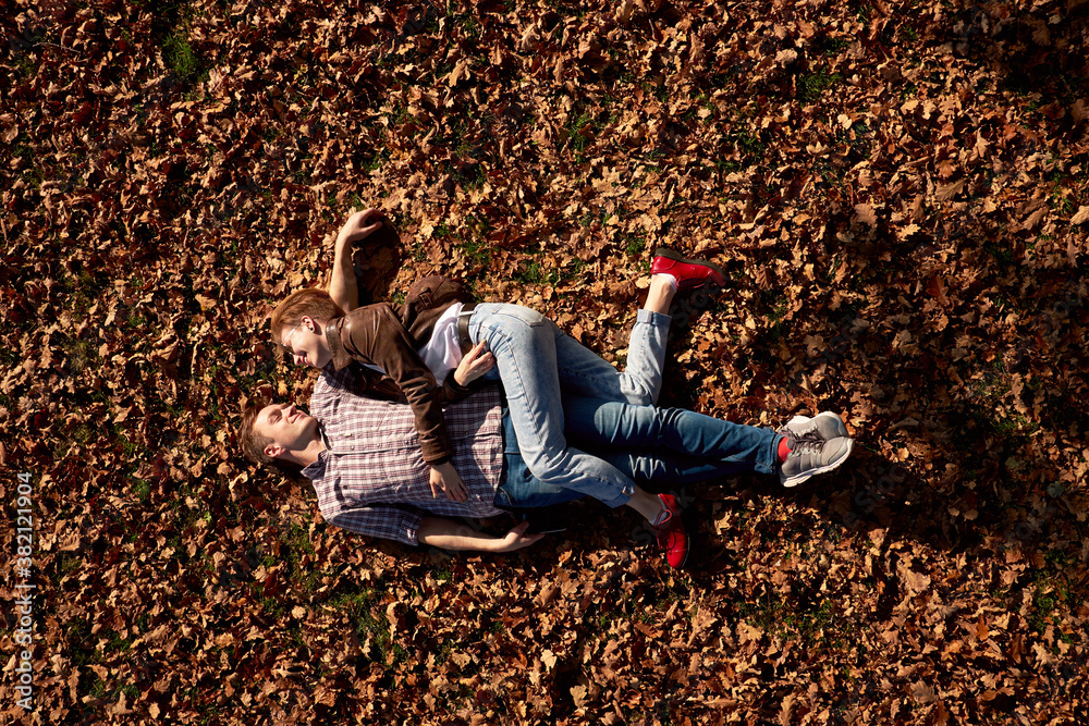 Happy attractive stylish young couple lying on the ground and hugging while walking in autumn park. Happy attractive stylish young couple lying on the ground and hugging while walking in autumn park.