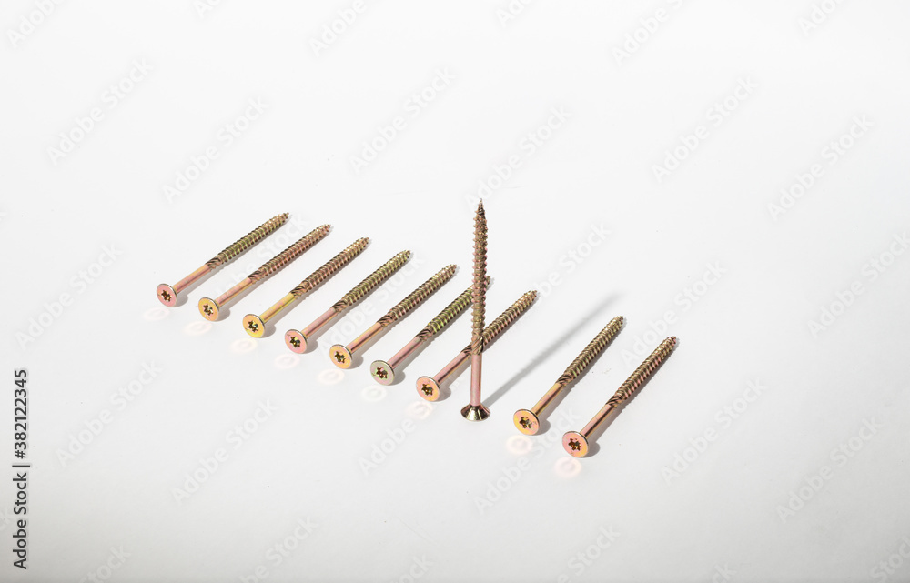Construction metal screws of gold color on a white background lie in a row, and one stands. Self-tapping screws as a background. Place for text Construction metal screws of gold color on a white background lie in a row, and one stands. Self-tapping screws as a background. Place for text