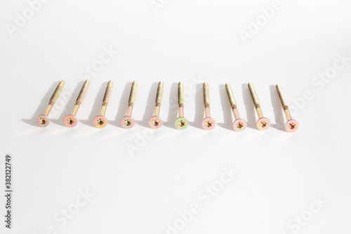 construction concept. Construction metal screws of gold color on a white background lie in a row  and one stands. Self-tapping screws as a background. Place for text