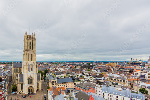 Aerial view of the Ghent cityscape, the facade of St Bavo Cathedral with its imposing tower surrounded by houses and buildings in the city center, cloudy day with a cloud covered sky in Belgium