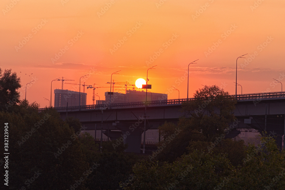 Astonishing sunrise in downtown. Detailed view the structures of the concrete bridge. Big sun disk appears come out from the unfinished apartment building in the background. Autumn morning in Kyiv Astonishing sunrise in downtown. Detailed view the structures of the concrete bridge. Big sun disk appears come out from the unfinished apartment building in the background. Autumn morning in Kyiv