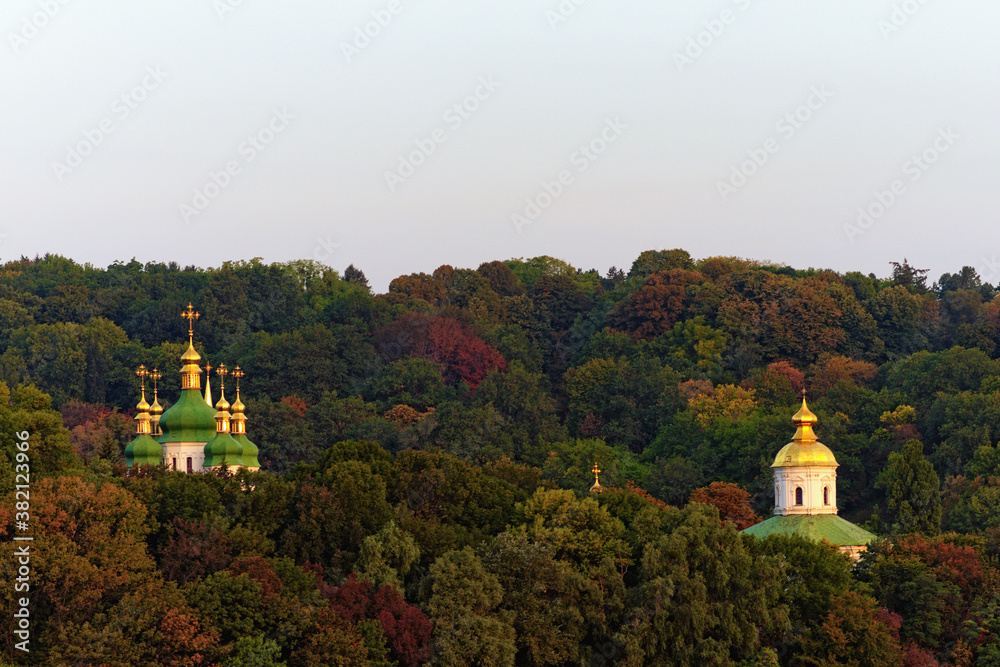 Astonishing morning autumn landscape view of famous Kyiv?s hills against blue sky. The domes Saint George's Cathedral and ancient Michael's Cathedral of Vydubychi Monastery over the old trees. Kyiv