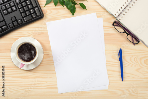 Flat lay, top view office table desk. Workspace with blank sheet of paper, keyboard, office supplies, pencil, green leaf, and coffee cup on wooden table background
