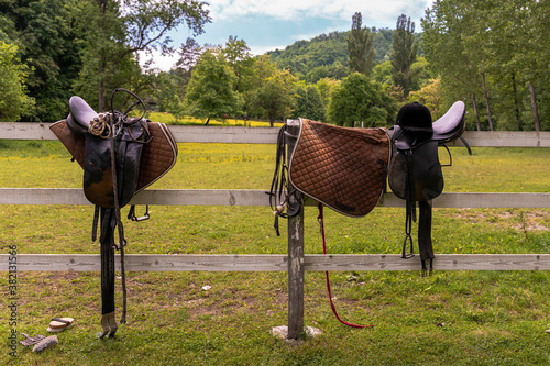 Brown leather equestrian sport equipment and accessories hanging on fence of a ranch photo