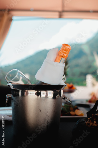 a bottle of sparkling wine with glasses in an ice bucket on a served table on the terrace on a summer day