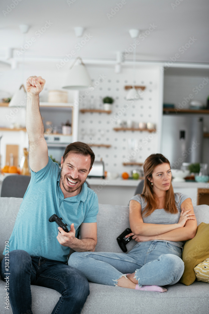 Husband and wife playing video game with joysticks in living room. Loving couple are playing video games at home Husband and wife playing video game with joysticks in living room. Loving couple are playing video games at home