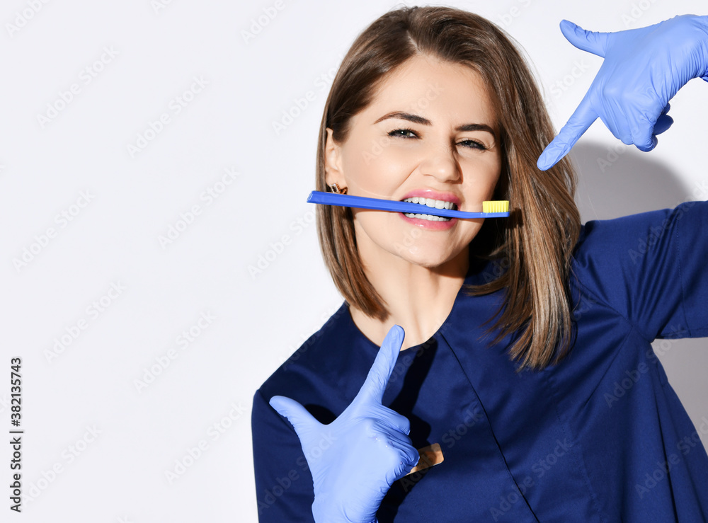 Portrait of young beautiful woman dentist with toothbrush in her white healthy teeth mouth pointing with fingers at it Portrait of young beautiful woman dentist with toothbrush in her white healthy teeth mouth pointing with fingers at it