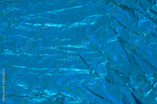 The texture of a thin crumpled sheet of blue foil. Crumpled foil background. Shiny blue foil background. copy space. Selective focus. Blurred background. flatlay