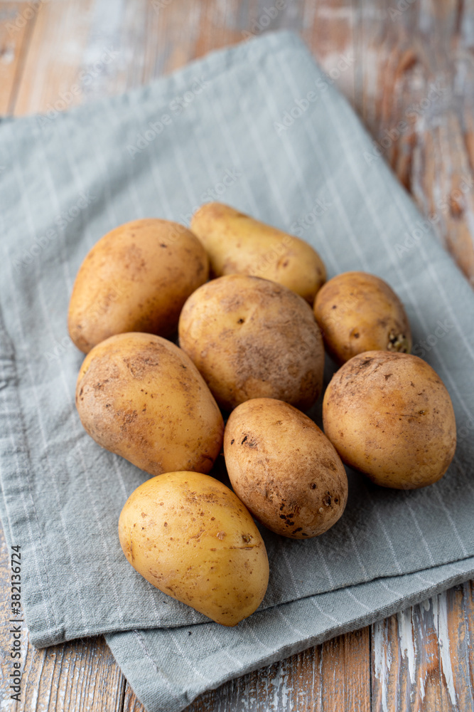 Raw unpeeled potato on light wooden kitchen table with cotton cloth aside, close up, catalogue photo Raw unpeeled potato on light wooden kitchen table with cotton cloth aside, close up, catalogue photo