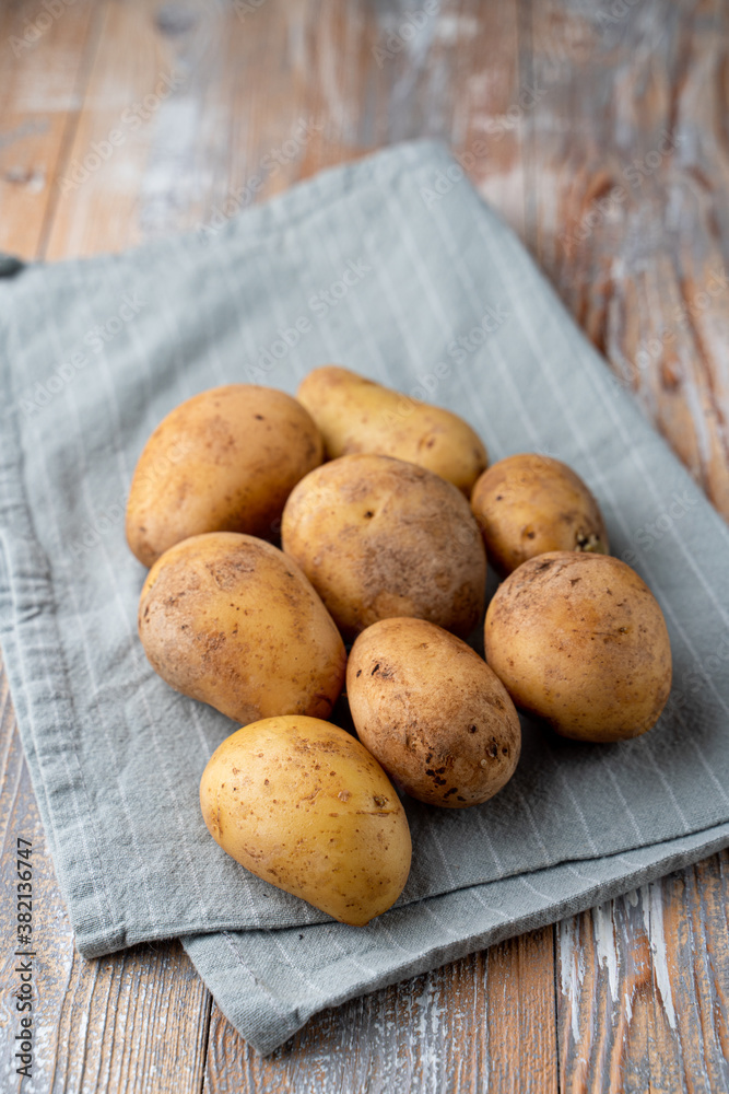 Raw unpeeled potato on light wooden kitchen table with cotton cloth aside, close up, catalogue photo Raw unpeeled potato on light wooden kitchen table with cotton cloth aside, close up, catalogue photo