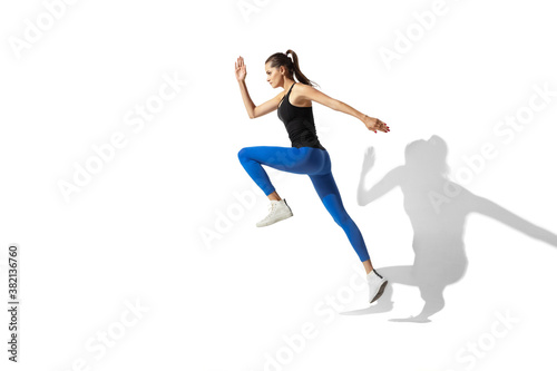 High up. Beautiful young female athlete stretching, training on white studio background, portrait with shadows. Sportive fit model in motion and action. Flexibility, healthy lifestyle, style concept.