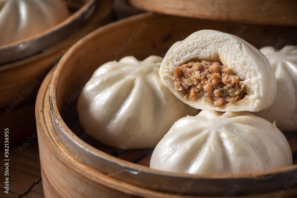 Fototapeta premium Delicious baozi, Chinese steamed meat bun is ready to eat on serving plate and steamer, close up, copy space product design concept.