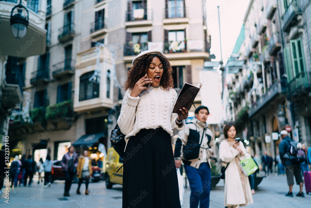 Fototapeta premium Emotional expressive dark skinned female having emotional cellular conversation with operator screaming, angry african american woman irritated with problems talking on mobile phone loudly on street