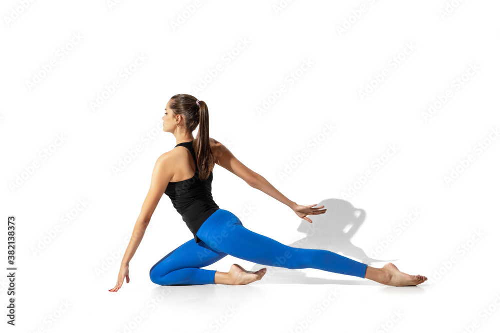 Light. Beautiful young female athlete stretching, training on white studio background, portrait with shadows. Sportive fit model in motion and action. Flexibility, healthy lifestyle, style concept.