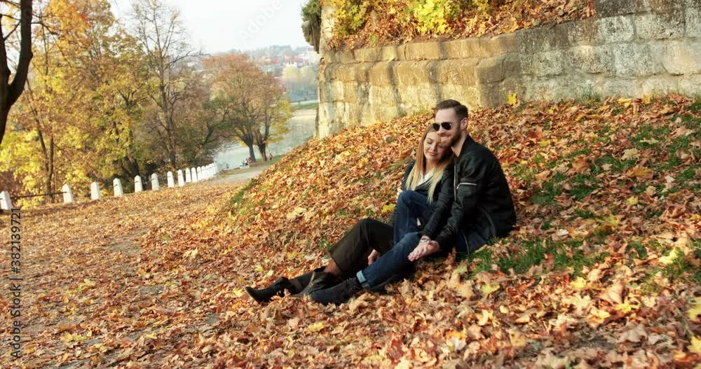 Beautiful autumn view with couple in love relaxes, caresses each other on lawn Beautiful autumn view with couple in love relaxes, caresses each other on lawn