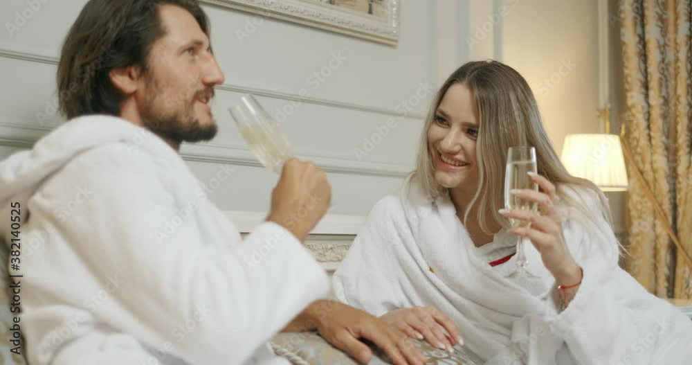 Affectionate couple toasting with champagne lying on their bed. Hotel, travel, relationships and happiness concept - smiling couple with champagne glasses in room Affectionate couple toasting with champagne lying on their bed. Hotel, travel, relationships and happiness concept - smiling couple with champagne glasses in room