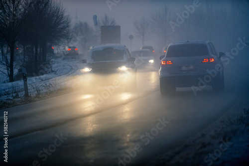 Luminous car headlights in the twilight in fog. © Anna