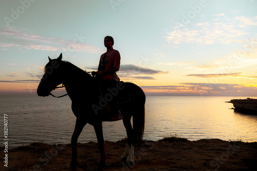 Silhouette of a girl on a horse against the background of the sea and the gentle sunset sky. © FO_DE