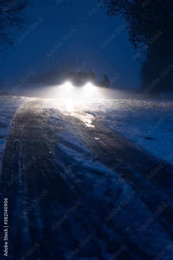 Naklejka premium Luminous car headlights in the night in fog on snow track.