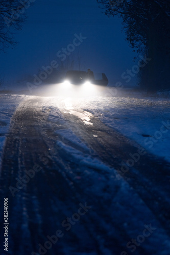Luminous car headlights in the night in fog on snow track.