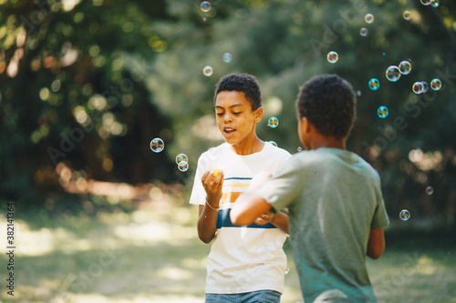 Cute african boy blowing bubbles outdoors with his friend and having fun on beautiful sunny day.