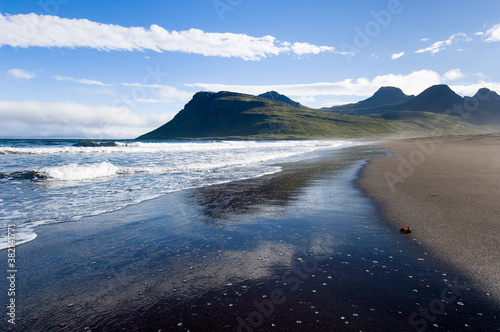 Black beach on the east coast of Iceland in sunlight with sky reflection.