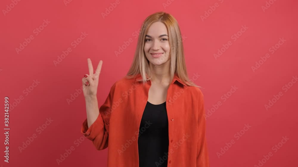 Close up of a smiling charming young woman showing peace sign over red background. Close up of a smiling charming young woman showing peace sign over red background.