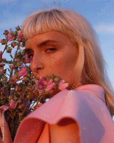 Portrait of girl with bangs with pink flowers . Model in pink dress hugs flowers