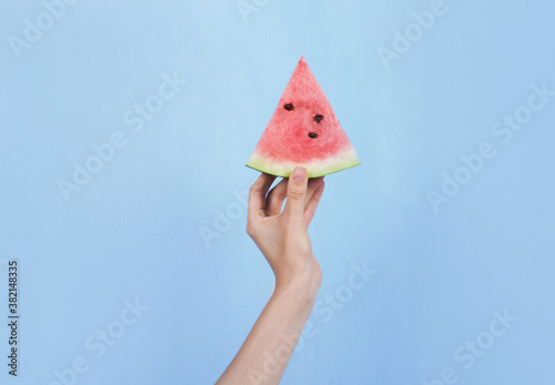 Hand holding slice of ripe watermelon on blue background